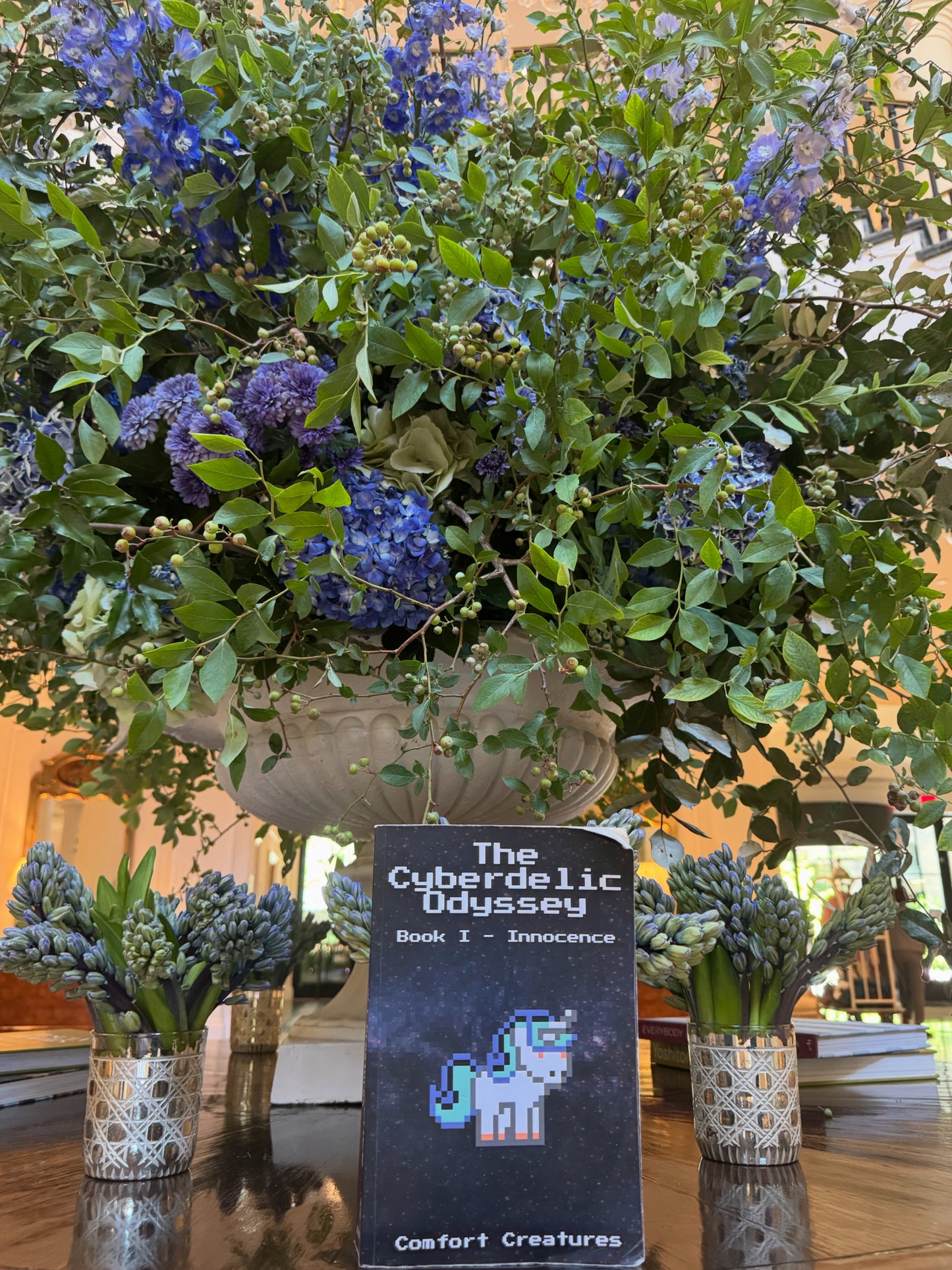 Floral arrangement with a book titled 'The Cubedelic Odyssey' on a reflective surface.
